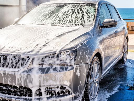 Coche reluciente recién lavado en el lavadero de Sagunto con espuma blanca y reflejos brillantes bajo el sol mediterráneo