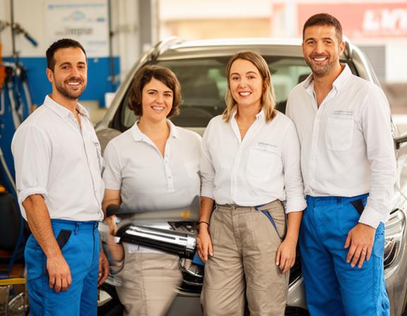 Equipo de profesionales de Carpio's Limpio en el lavadero de Sagunto, con uniforme y productos de limpieza, sonriendo junto a un coche recién lavado